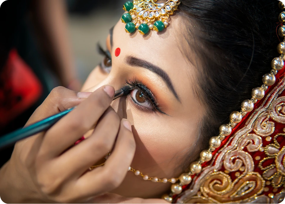 Bride getting eye makeup applied, traditional attire.